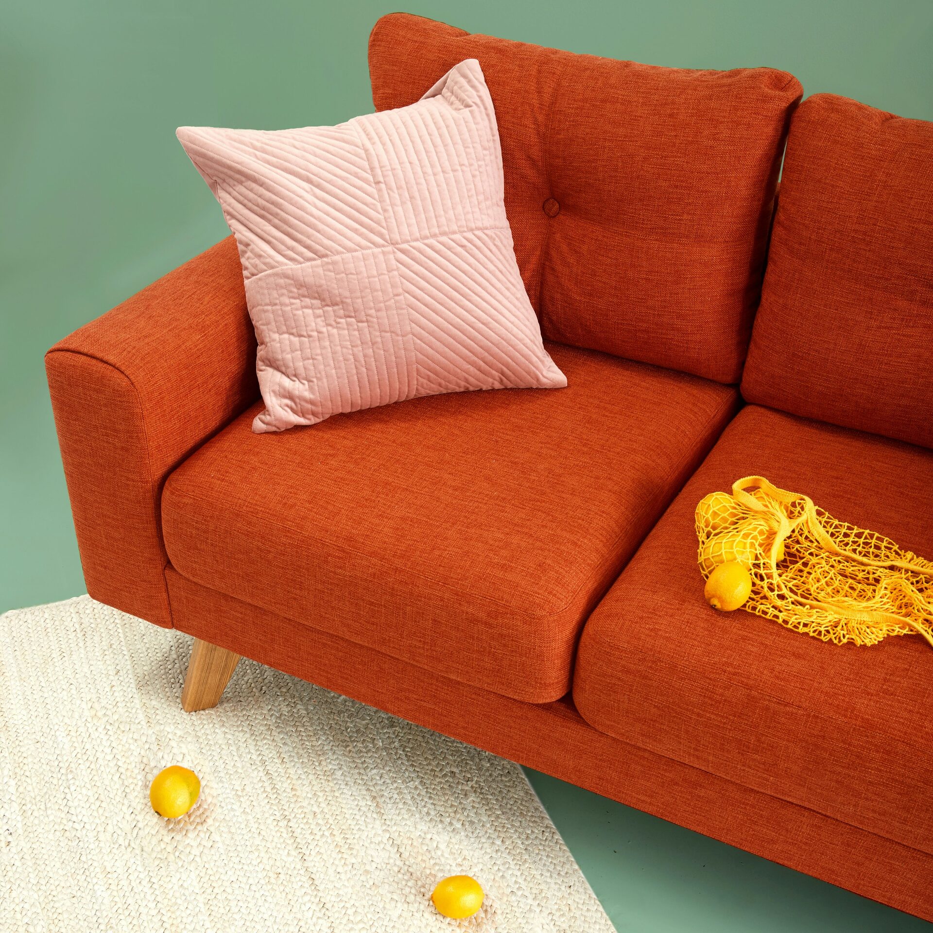 Orange sofa with a pink pillow, mesh bag, and lemons in a living room