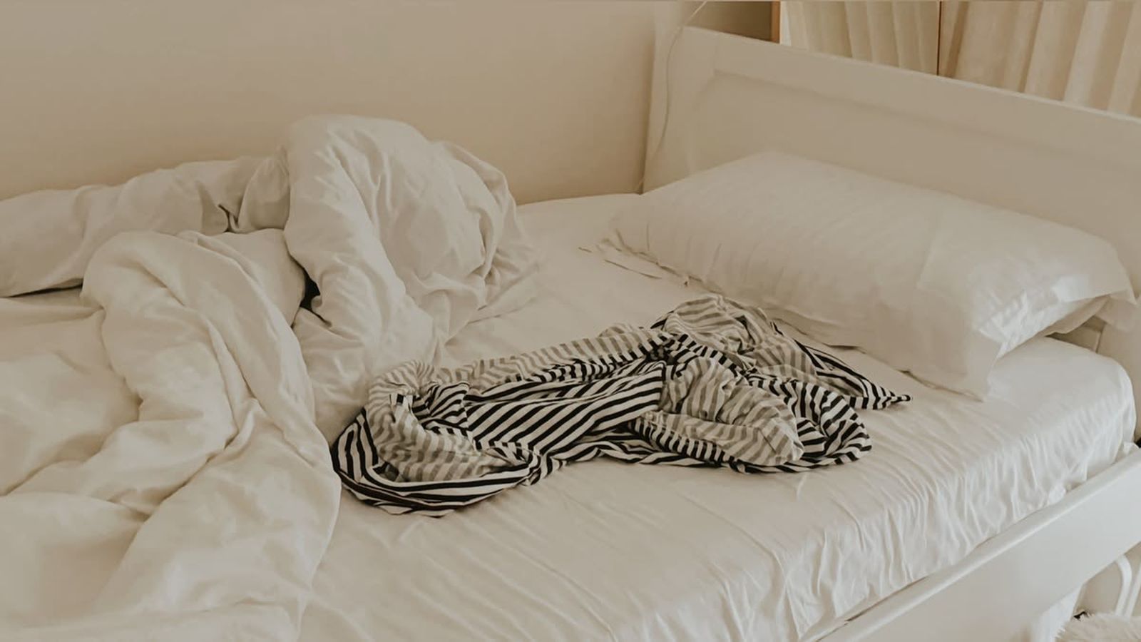 Unmade bed with rumpled white linens and a striped shirt