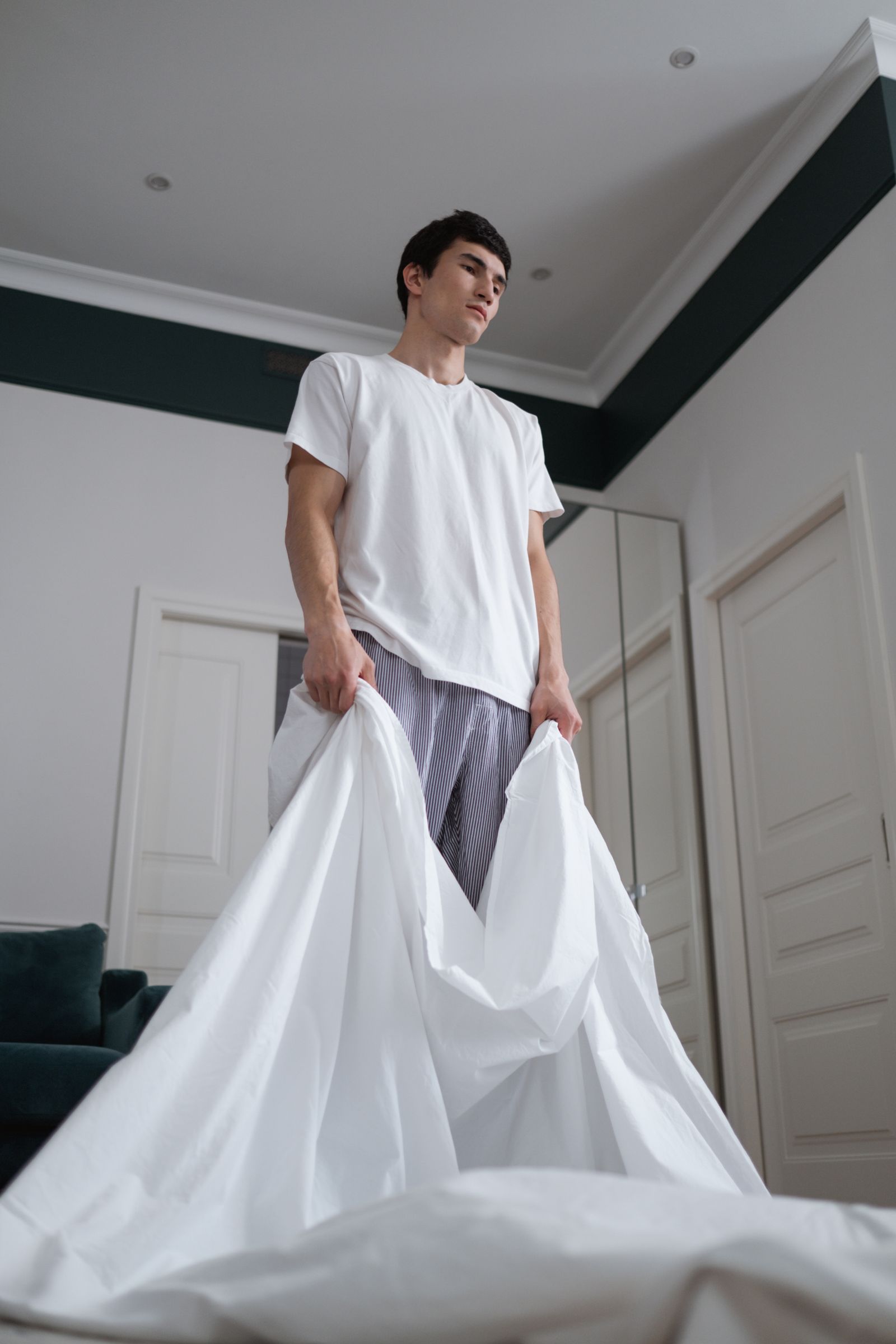 Person holding up a white bed sheet in a bedroom