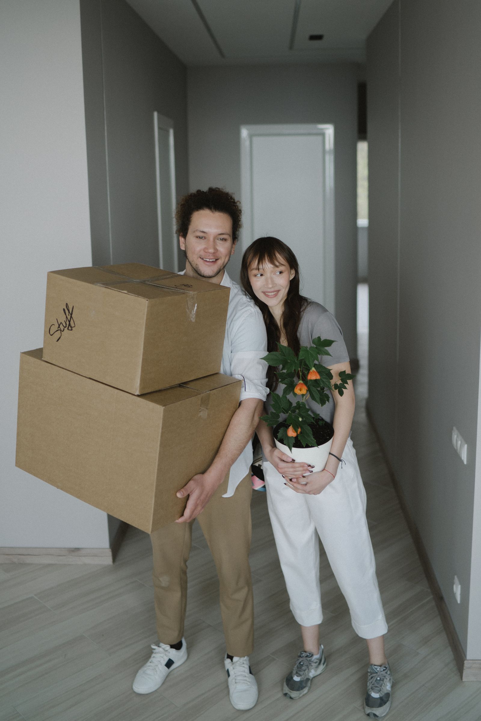Two people carrying moving boxes and a plant into a home