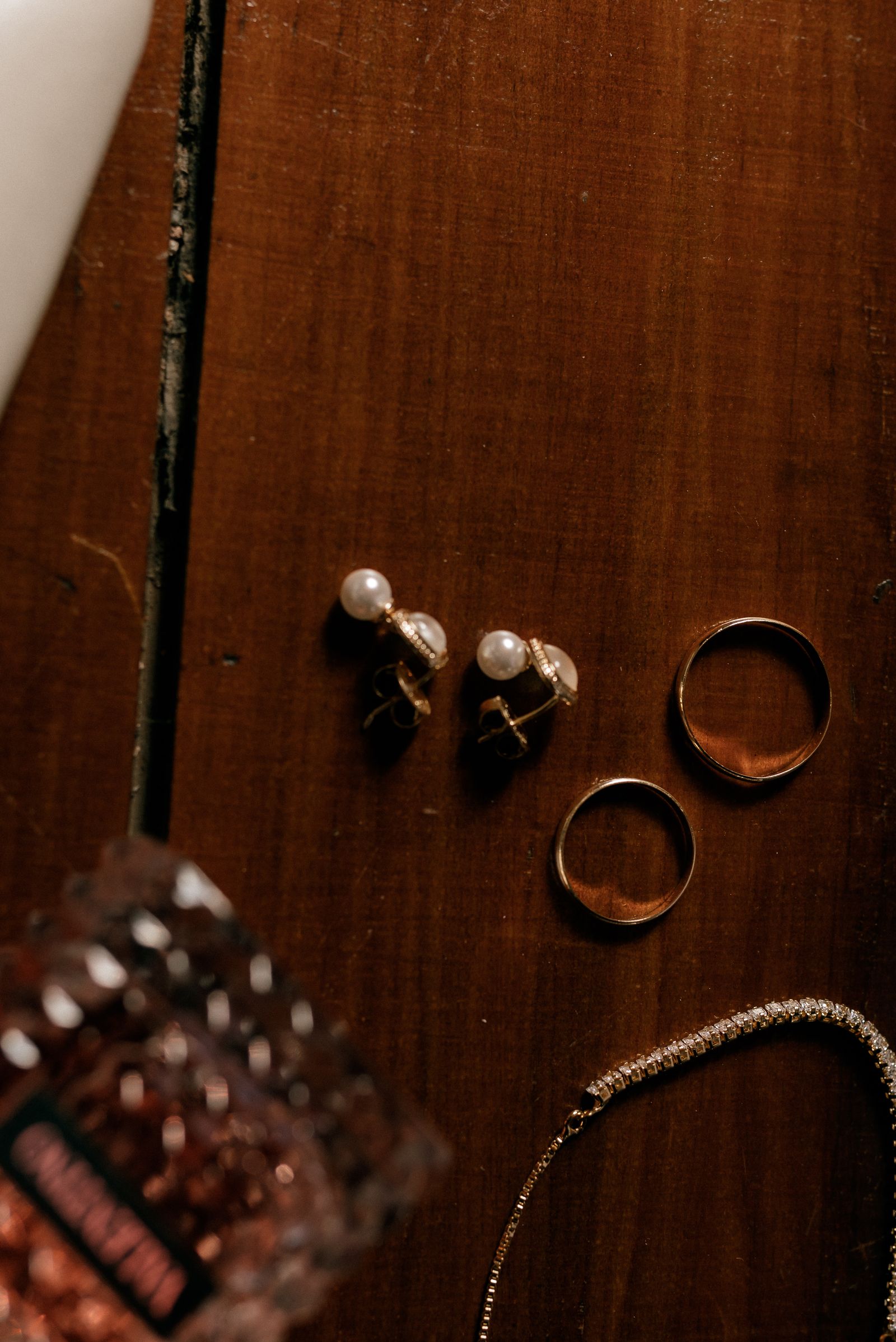 Pearl earrings, gold rings, and a necklace arranged on a wooden table
