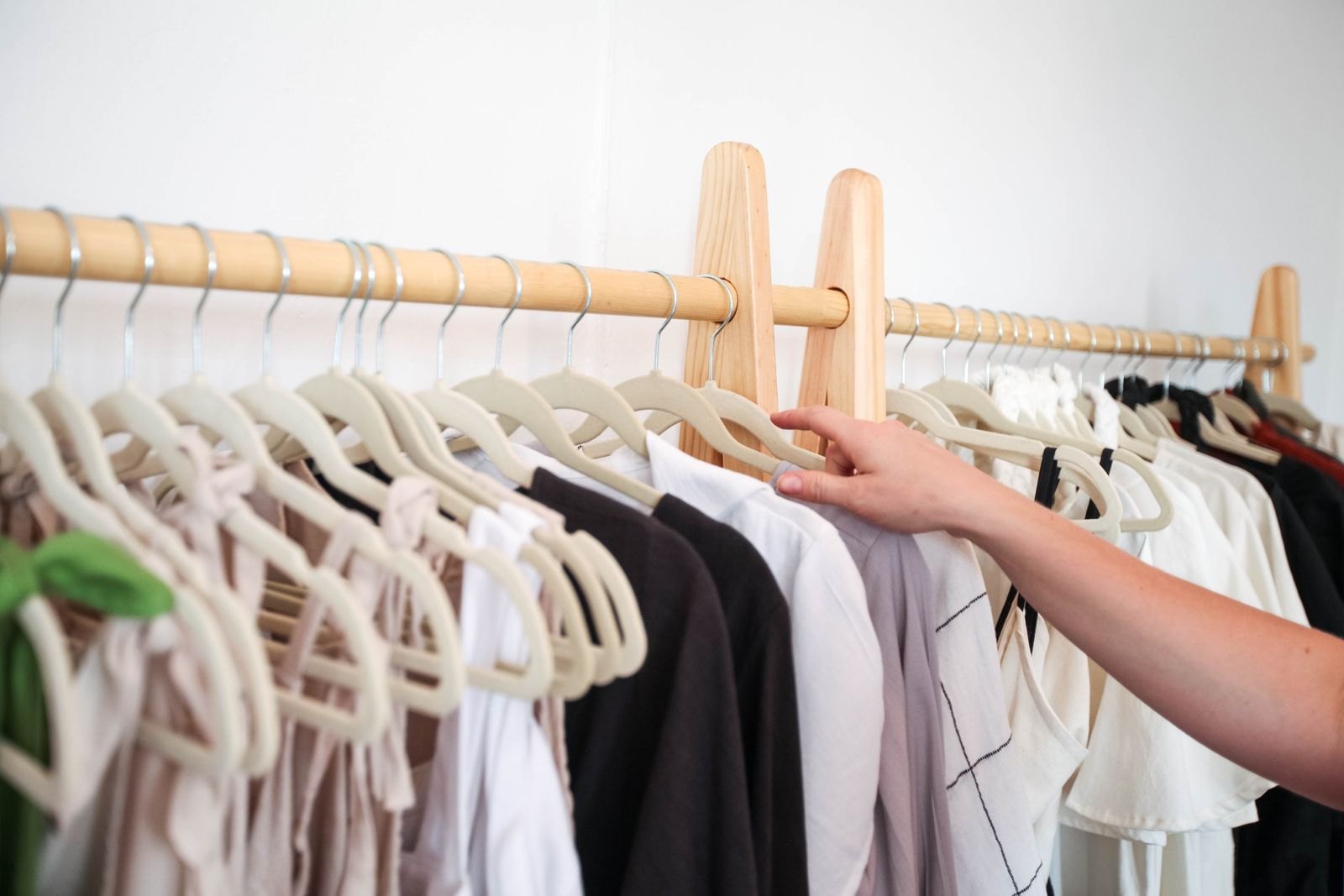 A hand reaching for a shirt on a wooden clothing rack