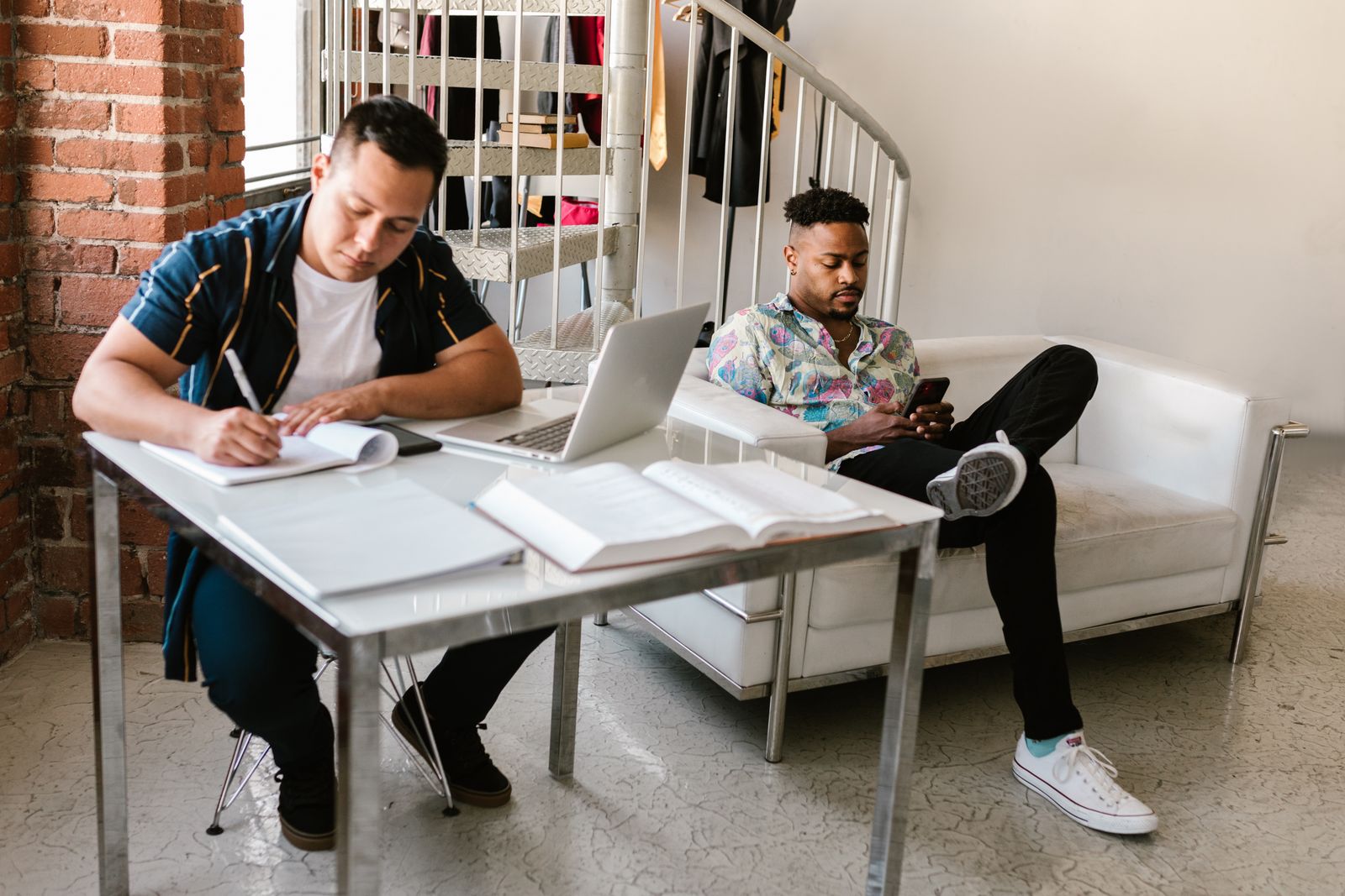 Two young men with books and a laptop in a loft apartment