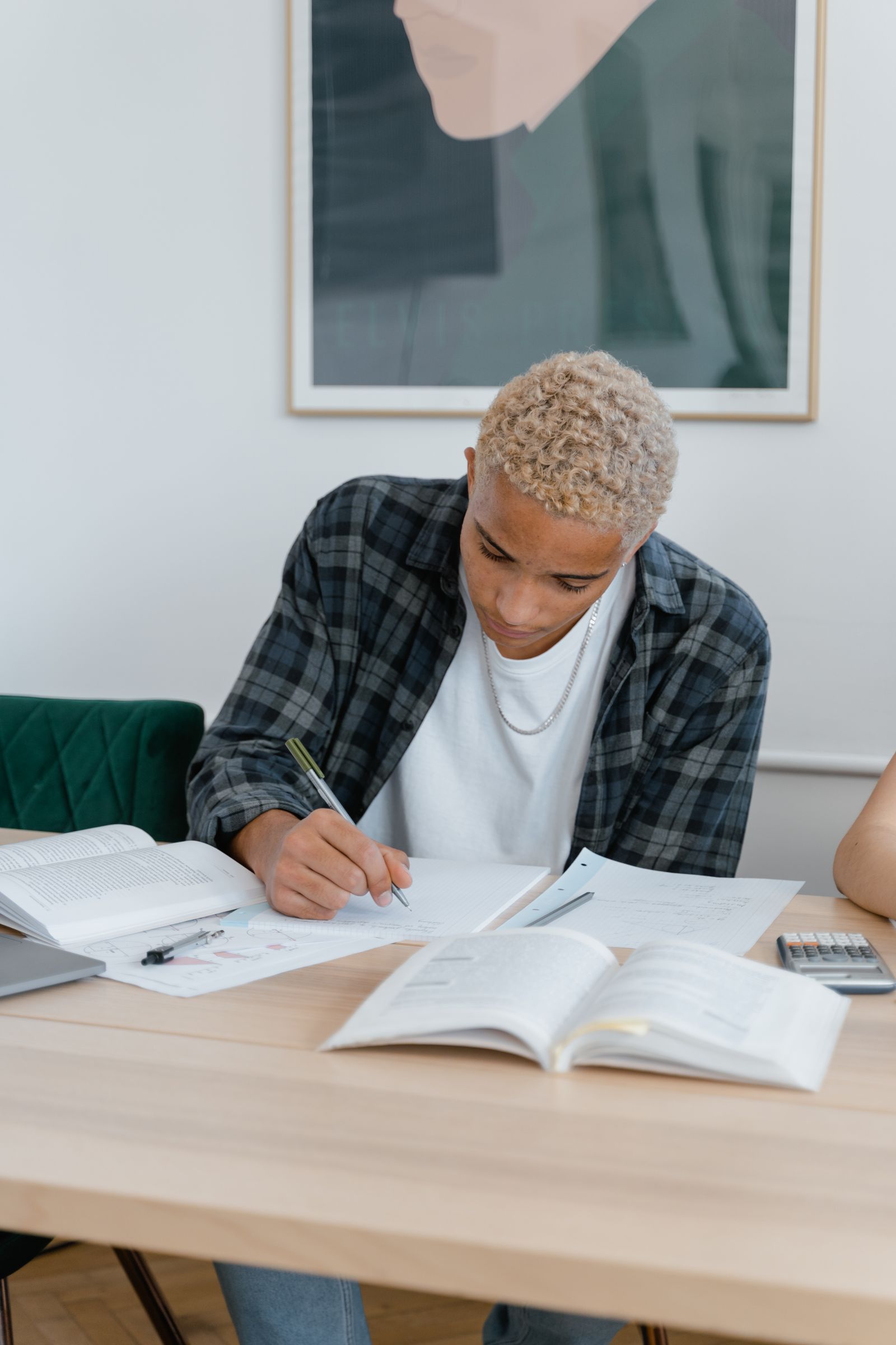 A student writing at a desk surrounded by open books