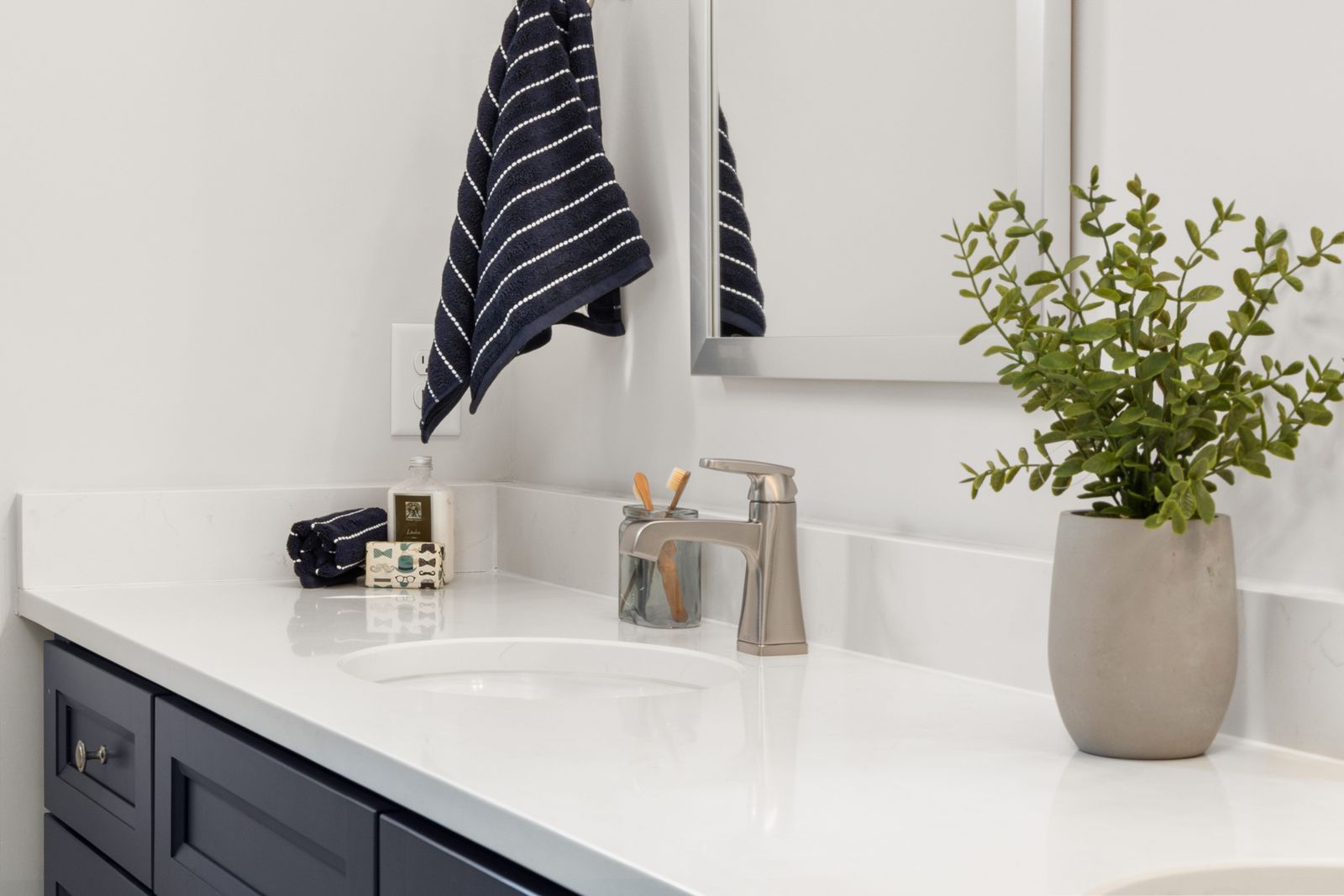 Bathroom vanity with a brushed nickel faucet, striped towel, and potted plant