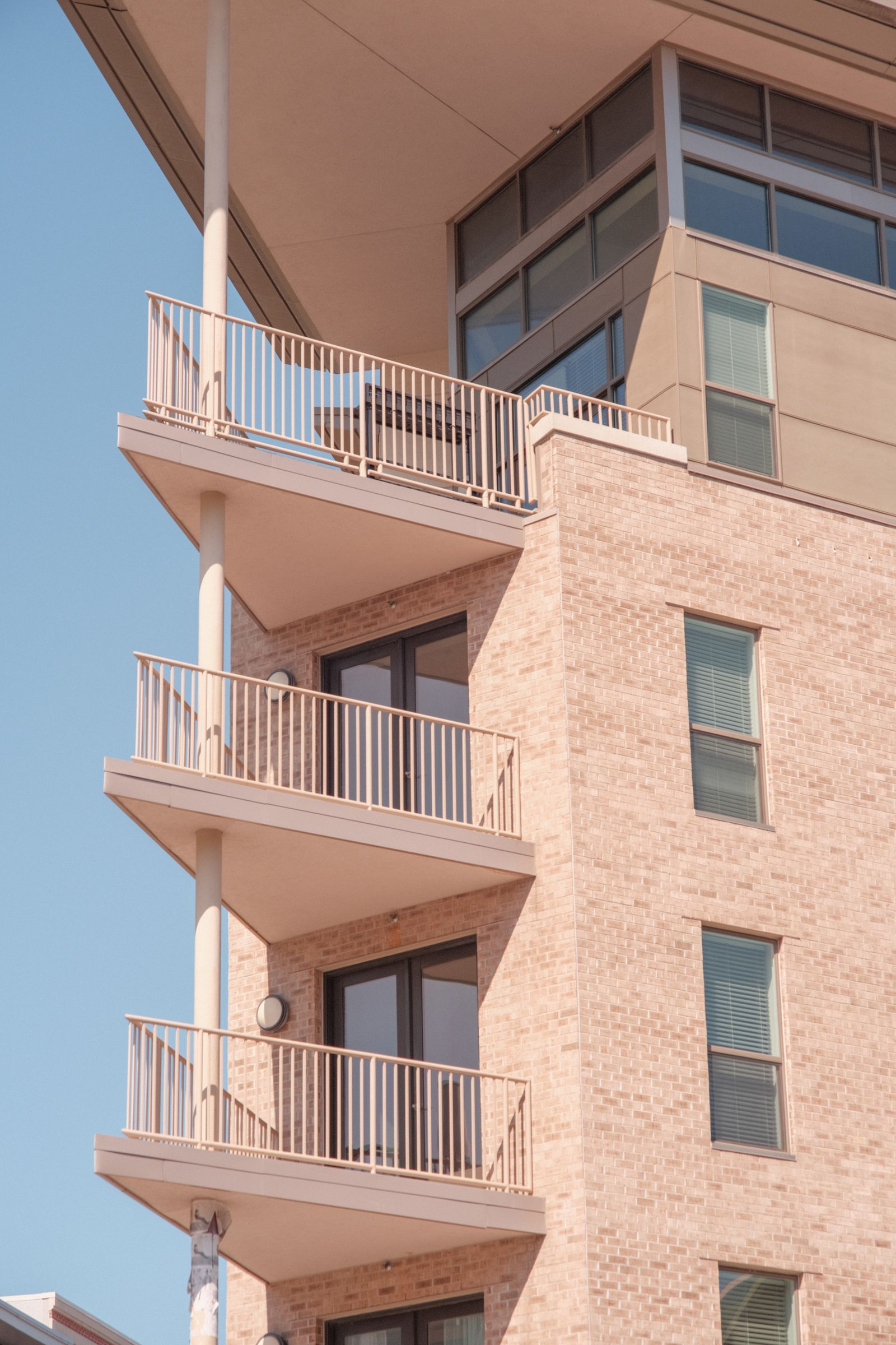 Corner of a brick apartment building with stacked balconies against a blue sky