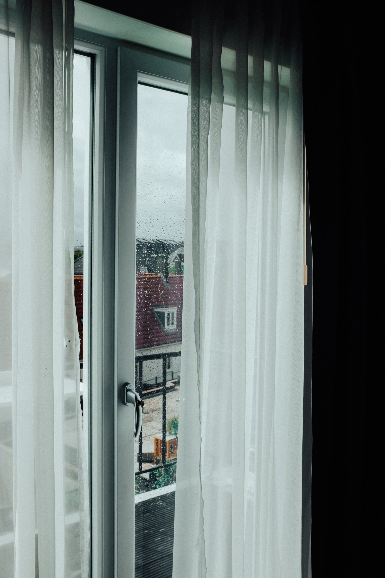 Window with white curtains and raindrops on the glass